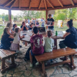 Predavačica sa fotografijom šišmiša u ruci predaje okupljenim ljudima za stolom ispred nje.